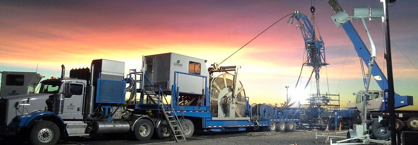 Oilfield coiled tubing truck and equipment operating at sunset with a dramatic sky in the background